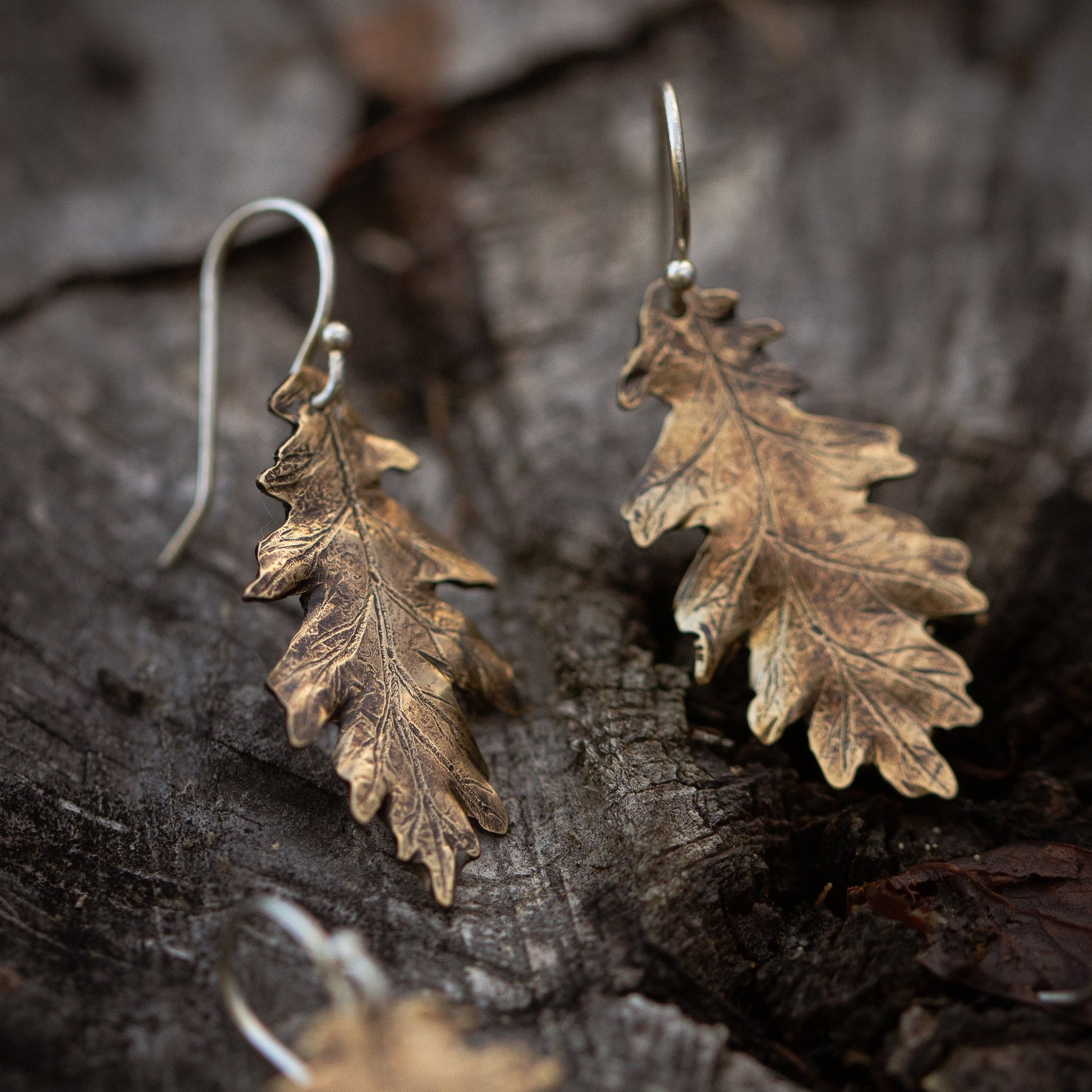 Bronze oak leaf-shaped earrings on a textured wooden surface
