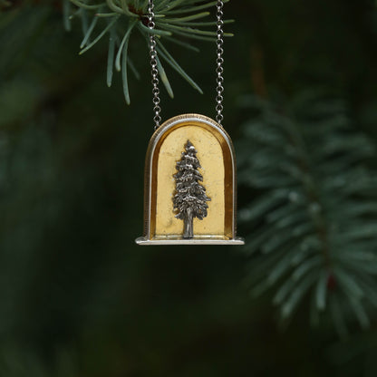 A sterling silver and 24k gold necklace in an arch shape featuring a layered sterlign silver redwood tree with a green tree background