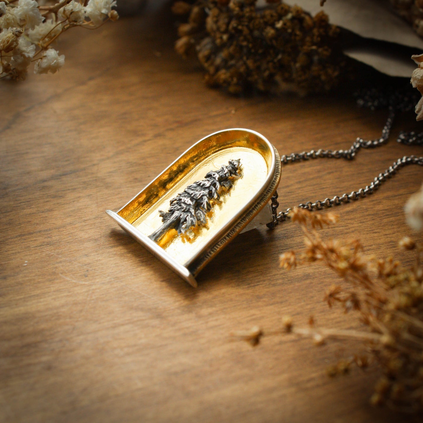 A sterling silver and 24k gold necklace in an arch shape featuring a layered sterlign silver redwood tree with a wood background