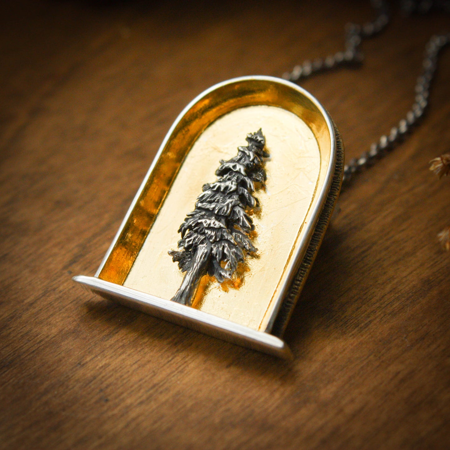A sterling silver and 24k gold necklace in an arch shape featuring a layered sterlign silver redwood tree with a wood background